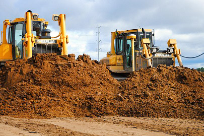 excavator digging the footings of a commercial construction, dump truck waiting to be loaded with earth dirt