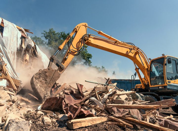 A yellow excavator is demolishing a pile of rubble on a residential property